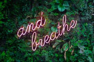 Rosa Neonschrift "and breathe" hängt an einer mit dichtem Grün bewachsenen Mauer